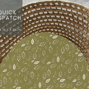 May include: A woven wicker basket with a green fabric liner featuring a white leaf pattern. The basket is empty and ready to be filled.