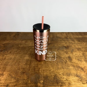 Puede incluir: Un vaso de acero inoxidable color oro rosa con tapa negra y una pajita rosa. El vaso tiene texto blanco que dice "You will never regret being kind".