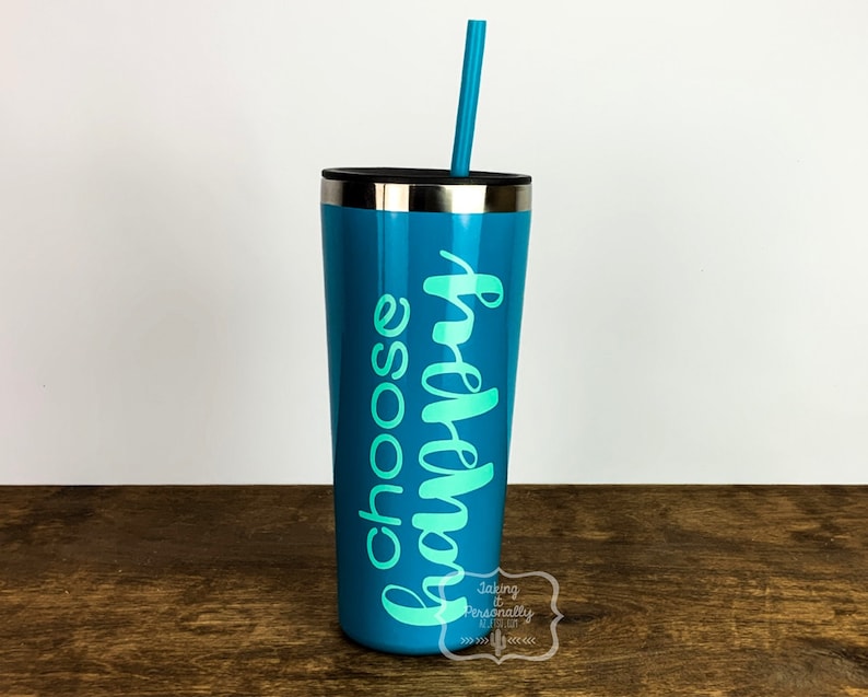 Puede incluir: Un vaso de color turquesa con tapa plateada y una pajita turquesa. El vaso tiene las palabras "choose happy" escritas en una escritura turquesa.