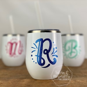Könnte beinhalten: Weiße, stiellose Weingläser mit silbernen Rändern und Strohhalmen. Jedes Glas hat einen anderen Anfangsbuchstaben in einem glitzernden Design: blaues "R", rosa "M" und grünes "B". Die Gläser sind personalisiert.