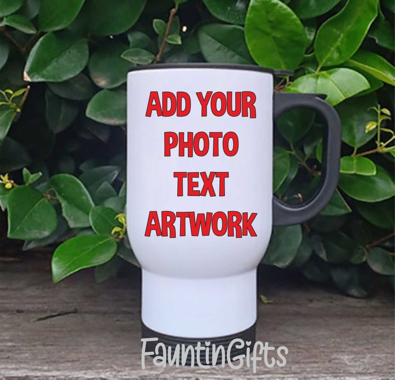 May include: A white travel mug with a black handle and rim. The mug features the red text "ADD YOUR PHOTO TEXT ARTWORK". The mug is set against a backdrop of green foliage and a wooden surface.