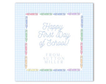 以下が含まれることがあります： 青と白のギンガムチェックの背景に、カラフルなクレヨンで縁取られたデザイン。カードの中央には「Happy First Day of School!」の文字。その下に「From: Sutton Miller」と記載されています。