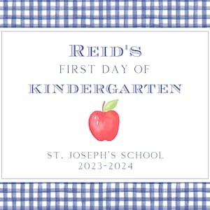 May include: A blue and white gingham background with a white rectangle in the center. The rectangle has the text "Reid's First Day of Kindergarten" with a red apple illustration. Below the text is "St. Joseph's School 2023-2024".