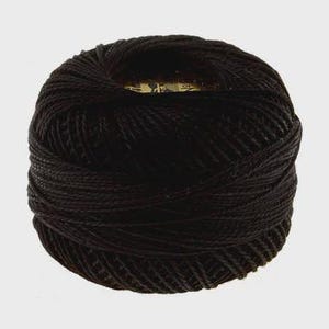 May include: A tightly wound ball of black thread, likely cotton or a similar fiber, is centered against a plain, light background. The thread is uniformly dark, with visible strands creating a textured surface. The ball's shape is round and compact.