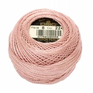 May include: A ball of DMC Perle cotton thread in a soft pink color. The label indicates it is size 8, color 224, and made in France. The thread is tightly wound, showing the texture of the cotton.