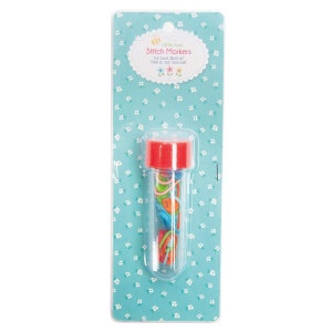 May include: A package of colorful stitch markers in a clear tube with a red cap. The package is on a light blue background with a white floral pattern. Text on the package reads "100% Cute Stitch Markers by Lori Holt of Bee in my Bonnet."