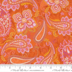 May include: Close-up of a fabric with a vibrant orange background and a paisley pattern. The design features large paisley shapes and floral elements in shades of pink, orange, and yellow. The fabric is measured with a ruler.