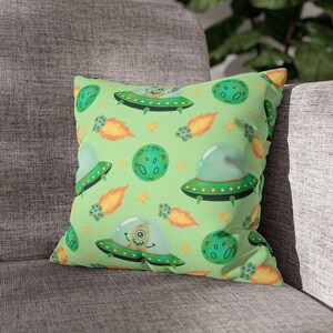 Op de afbeelding: Een vierkant decoratief kussen met een lichtgroene achtergrond. Het heeft een herhaald patroon van cartoon UFO's, planeten, sterren en kometen. De UFO's zijn groen met een heldere koepel en de planeten zijn groen met kraters.