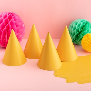 May include: Four yellow party hats on a pink background with two honeycomb balls, one pink and one green.