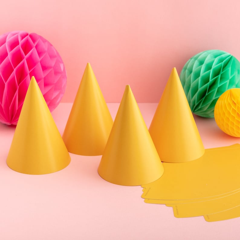 May include: Four yellow party hats on a pink background with two honeycomb balls, one pink and one green.