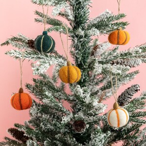May include: A snowy artificial Christmas tree decorated with felt pumpkin ornaments in orange, yellow, and white, and a green felt ornament.