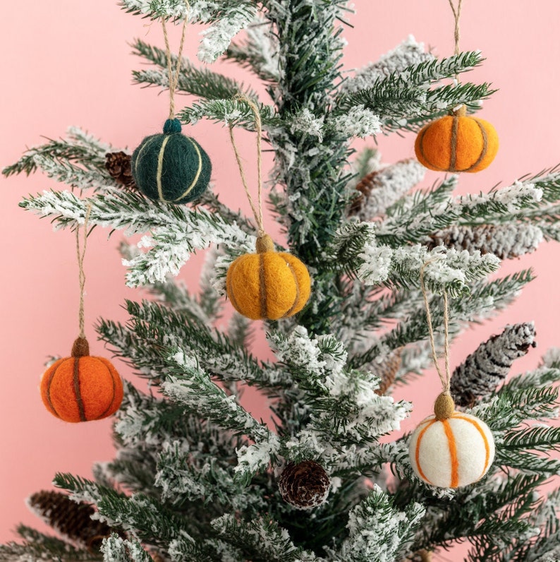 May include: A snowy artificial Christmas tree decorated with felt pumpkin ornaments in orange, yellow, and white, and a green felt ornament.