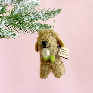 May include: A brown felt dog ornament with a green bow and a white felt bone in its mouth. The ornament has a wooden tag that says "Cassie's Second Christmas".