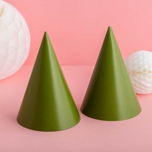 May include: Two green party hats on a pink background. The hats are made of paper and have a pointed tip.