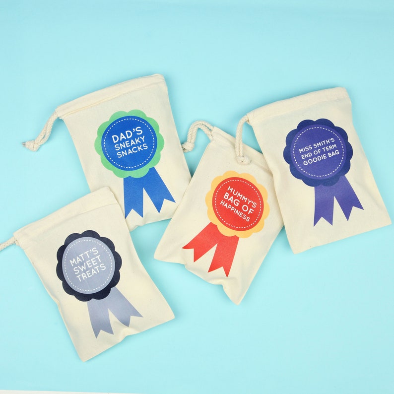May include: Four off-white drawstring bags with colorful ribbon designs. Text on the bags reads: "Dad's Sneaky Snacks", "Mummy's Bag of Happiness", "Matt's Sweet Treats", and "Miss Smith's End of Term Goodie Bag".