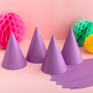 May include: Purple party hats with matching purple paper crowns. The hats are made of paper and have a cone shape. The crowns are flat and have a scalloped edge.
