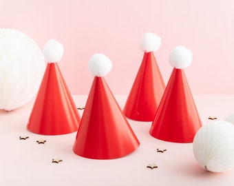 Peut inclure: Quatre chapeaux de Père Noël rouges avec des pompons blancs sur un fond rose. Les chapeaux sont disposés en rangée, avec deux à l'avant et deux à l'arrière. De petites étoiles en bois sont éparpillées autour des chapeaux.