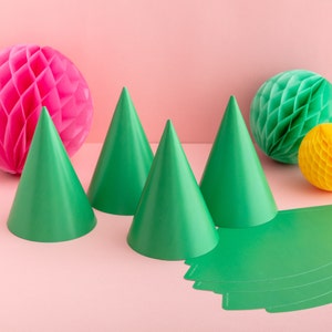May include: Four green party hats on a pink background with two honeycomb balls, one pink and one green, and a yellow honeycomb ball.