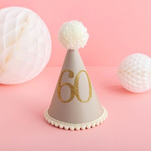 May include: A grey party hat with a white pom-pom on top and the number 60 in gold glitter on the front.