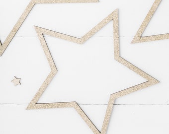 May include: Five gold glitter star shapes on a white background. The stars are arranged in a pattern with one large star in the center and four smaller stars around it.