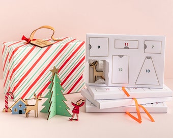 May include: A white cardboard advent calendar with numbered doors, a red and green striped box with a wooden tag that says "Merry Christmas", and wooden ornaments including a Christmas tree, reindeer, and a candy cane.