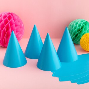 May include: Four blue party hats with a pink honeycomb ball and a green honeycomb ball in the background. There are also blue paper party hats on the table.