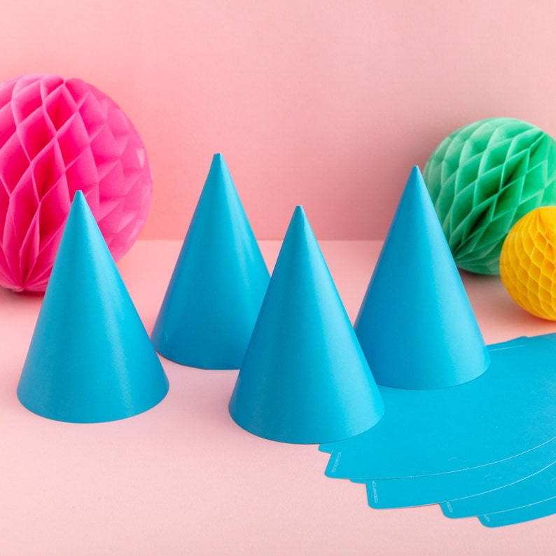 May include: Four blue party hats with a pink honeycomb ball and a green honeycomb ball in the background. There are also blue paper party hats on the table.