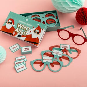 May include: A Christmas-themed game called "Who Am I?" with a red and green box and a Santa Claus illustration. The game includes a set of glasses with different names written on them, such as "David Attenborough" and "Margot Robbie".