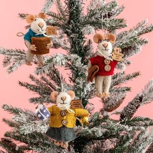 May include: Three felt mouse ornaments hanging on a snowy Christmas tree. Each mouse is wearing a different coloured sweater and holding a different gift. The ornaments have personalised tags with the text "You're on the nice list, Ben", "Miss. Miss Baby Dean", and "Tis the season to be merry".
