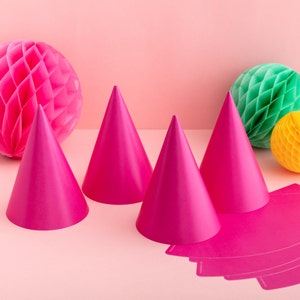 May include: Four pink party hats arranged on a pink background with two honeycomb balls, one green and one yellow.