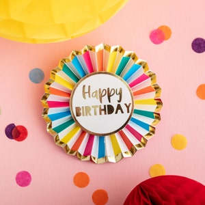 May include: A colorful, multi-layered paper rosette with gold trim and the words "Happy Birthday" in a gold circle in the center.