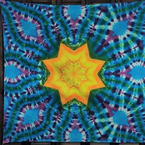 May include: A colorful tie-dye tapestry with a large yellow starburst in the center. The starburst has a repeating pattern of smaller stars within it. The background is a swirling pattern of blue, green, purple, and white.