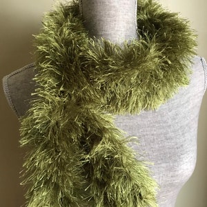 May include: A long, green, fuzzy scarf made of yarn. The scarf is draped around a mannequin's neck.