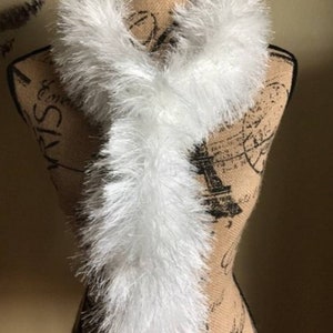 May include: A white fluffy scarf made of faux fur. The scarf is draped around a mannequin's neck.