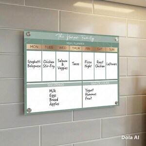 May include: A rectangular acrylic meal planner board with a sage green background and white grid lines. It features the text The Harper Family, Meal Planner, Shopping, and Snack Ideas. The board is mounted with four silver circular standoffs.
