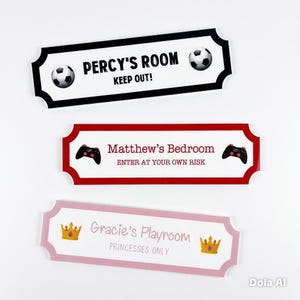 Puede incluir: Tres letreros decorativos para habitaciones con bordes negros, rojos y rosas. El letrero negro dice "PERCY'S ROOM KEEP OUT!" con balones de f&uacute;tbol. El letrero rojo dice "Matthew's Bedroom ENTER AT YOUR OWN RISK" con mandos de juego. El letrero rosa dice "Gracie's Playroom PRINCESSES ONLY" con coronas.
