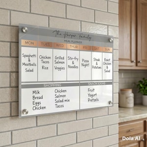 May include: A rectangular acrylic meal planner board with silver mounting hardware. The board features a weekly schedule from Monday to Sunday, a shopping list section, and a snack ideas section, all printed with black text on a white background.