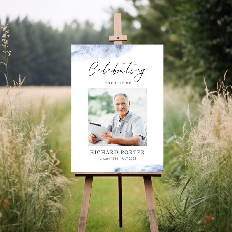 May include: A white sign on a wooden easel with the text "Celebrating the Life of" above a photo of a man holding a tablet. Below the photo is the name "RICHARD PORTER" and the dates "January 1936 - July 2025". The sign has blue watercolor accents.