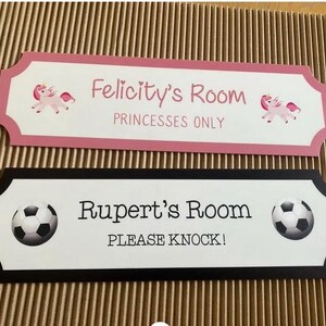 Puede incluir: Dos letreros de habitaci&oacute;n. El letrero superior es rosa y blanco, con el texto "Felicity's Room" y "Princesses Only", adem&aacute;s de gr&aacute;ficos de unicornios. El letrero inferior es blanco y negro, con el texto "Rupert's Room" y "Please Knock!", adem&aacute;s de gr&aacute;ficos de balones de f&uacute;tbol.