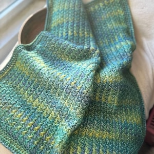 A crocheted blanket in shades of green and blue with a chevron pattern.