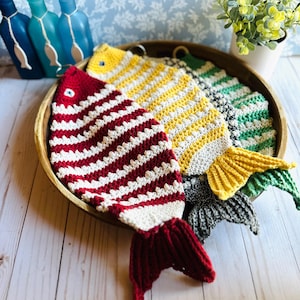 May include: Three crocheted fish ornaments in a wooden bowl. The fish are red and white, yellow and white, and green and black.