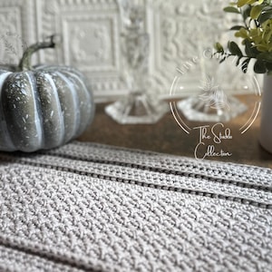 Könnte beinhalten: Ein grauer gehäkelter Tischläufer mit einem weißen Kürbis und einer Topfpflanze im Hintergrund. Der Text "Live Chuff Life" und "The Studio Collection" ist auf dem Bild zu sehen.