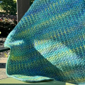 A close-up of a green, blue, and yellow crocheted blanket with a textured chevron pattern. it is an emotional support crochet stitch easy meditative with a calming fishtail appearance.