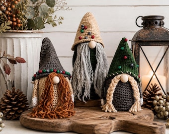 May include: Three handcrafted crochet gnomes featuring pointed hats in dark gray, tan, and forest green. The gnomes have wooden bead noses and yarn beards or braids in rust, gray, and cream colors, with small decorative beads on their hats.