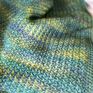 A close-up of a crocheted blanket with a green, blue, and yellow fishtail stitch pattern.