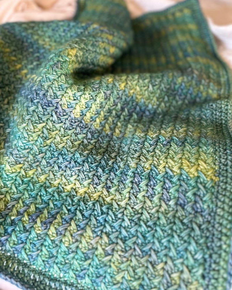 A close-up of a crocheted blanket with a green, blue, and yellow fishtail stitch pattern.