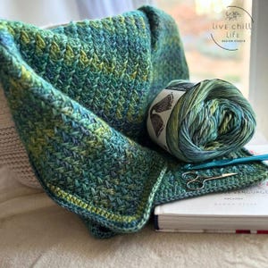 A close-up of a green, blue, and yellow crocheted blanket with a textured chevron pattern. it is an emotional support crochet stitch easy meditative with a calming fishtail appearance.