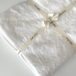 Könnte beinhalten: Ein weißer Leinenstoff, gefaltet und mit einem cremefarbenen Band gebunden. Das Band trägt den Aufdruck "Isle Linen".