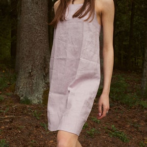 May include: A woman wearing a light purple linen dress in a forest setting.