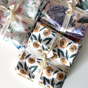 Puede incluir: Pilas de paquetes de tela con patrones florales y geométricos, atados con cinta de color crema y etiquetados "Isole Linen".